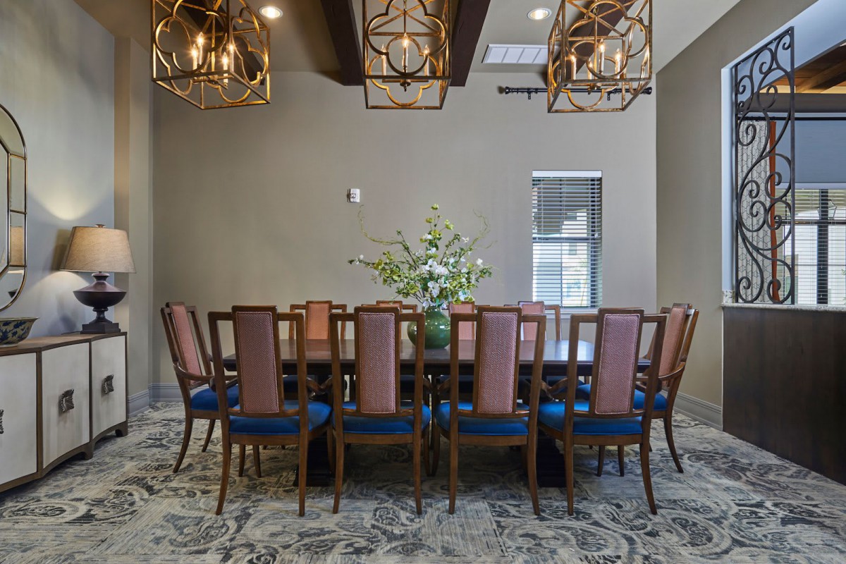 A sophisticated dining room with an elegant table and chairs, adorned with chandeliers and a central flower arrangement.