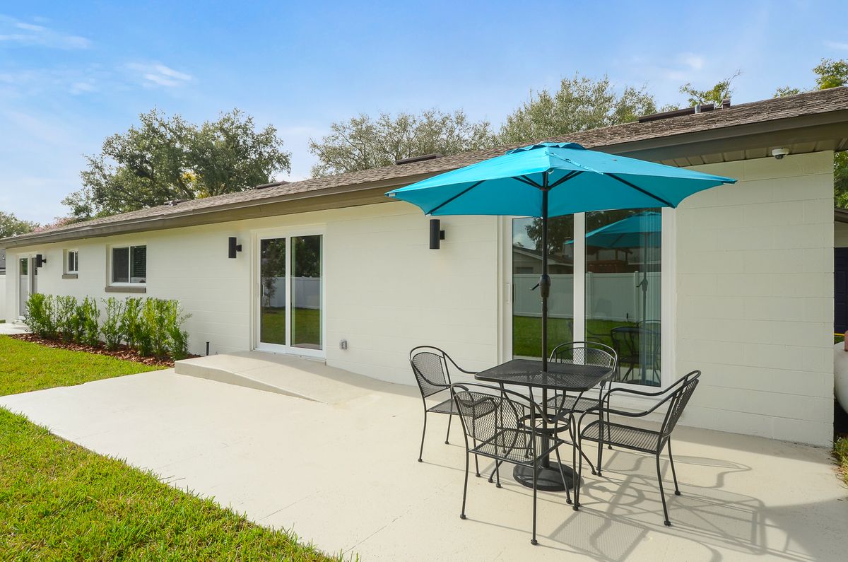 An inviting outdoor patio area with a table, chairs, and a bright blue umbrella beside a modern house.