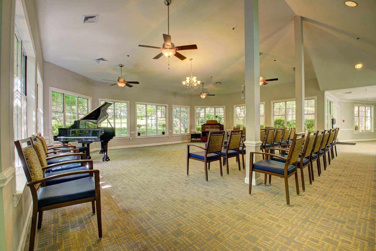 A spacious room with a grand piano, arranged chairs, large windows, and ceiling fans.