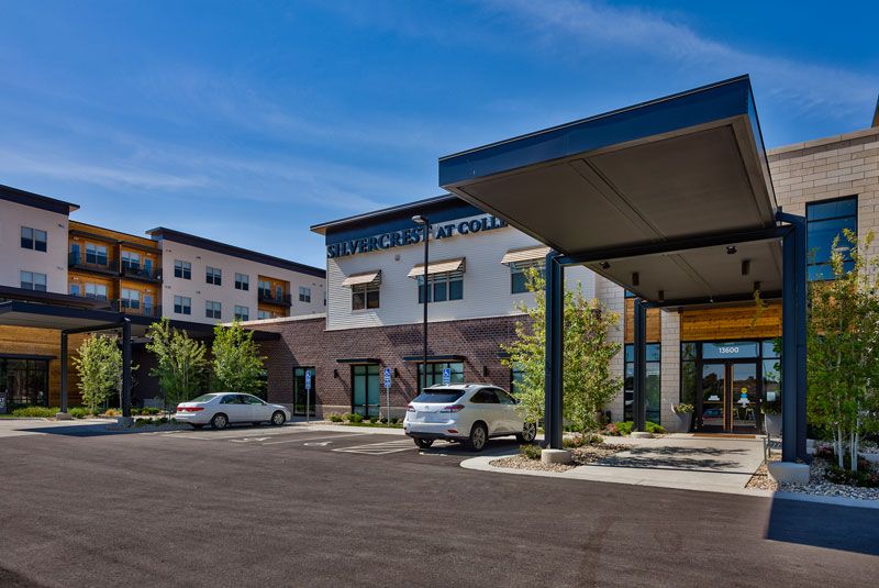 A modern commercial building with a parking lot and cars under a clear blue sky.