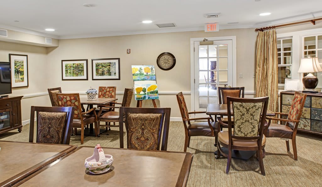 A cozy and well-decorated dining area with wooden tables and chairs, adorned with artwork and a wall clock.