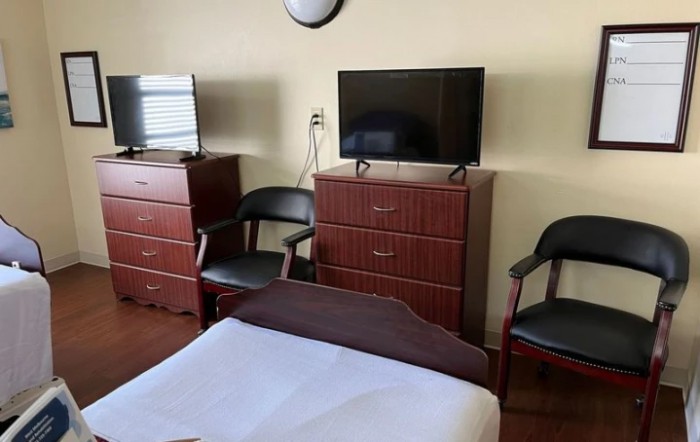 A simple hotel room with two televisions, dressers, and chairs.
