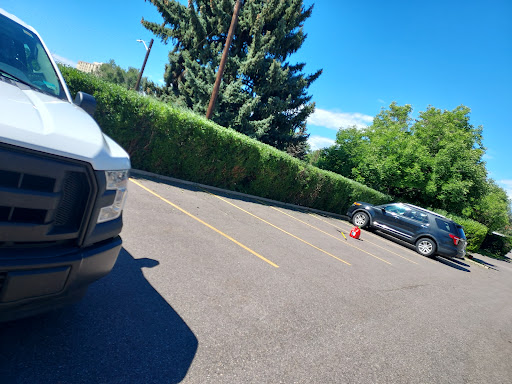 A view of a parking lot with two vehicles and lush greenery under a clear blue sky.