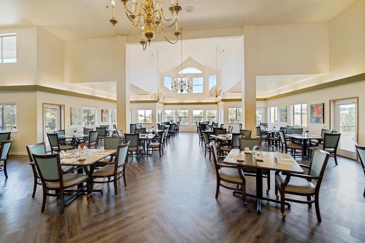 A spacious and elegantly designed restaurant dining area with several tables and chairs, featuring large windows and a central chandelier.