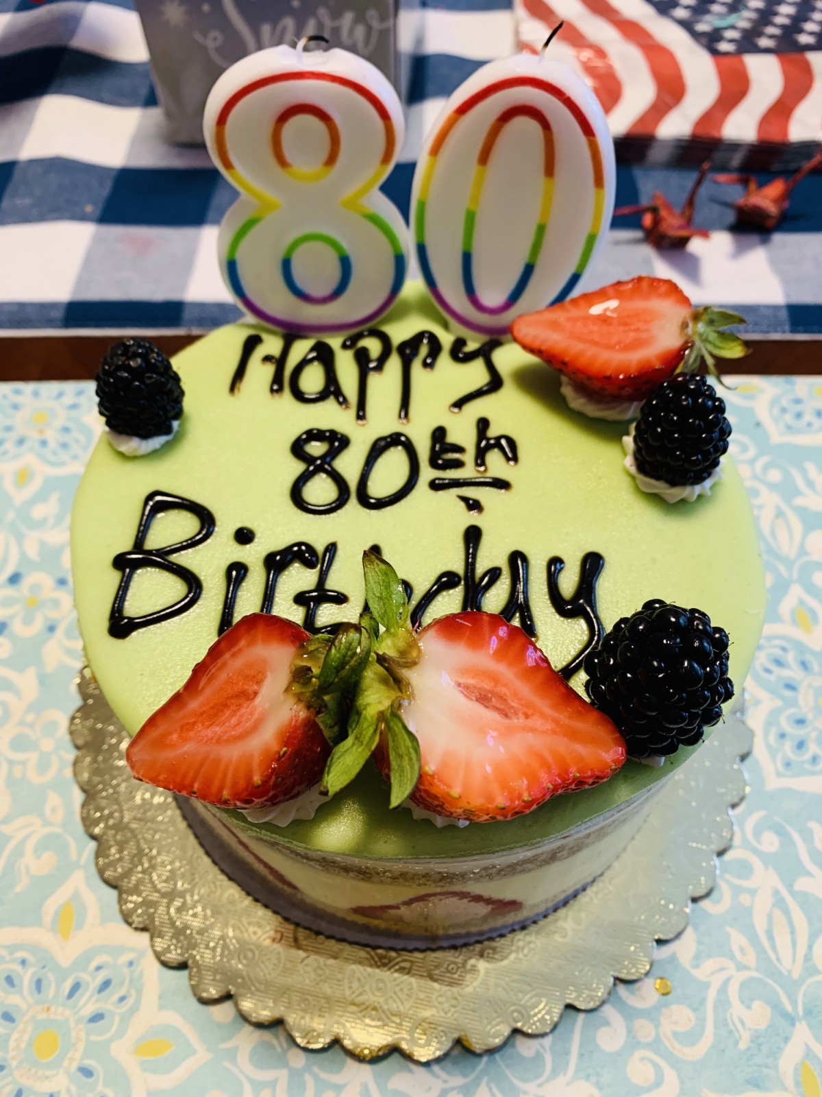 A colorful 80th birthday cake decorated with fruit and number candles.