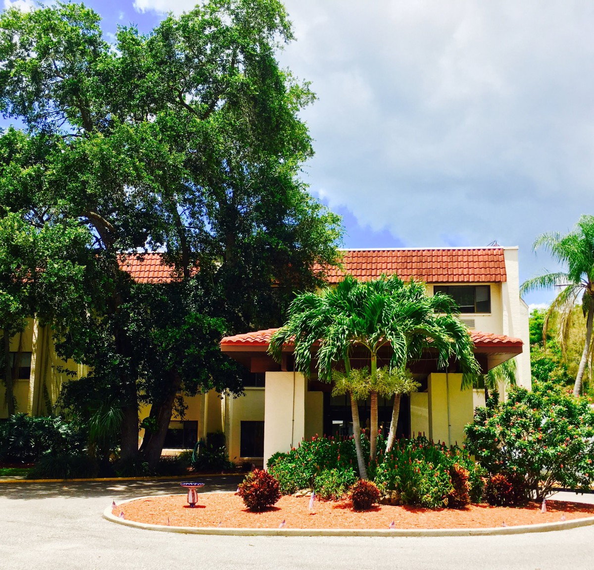 A tropical building surrounded by lush greenery and palm trees under a partly cloudy sky.