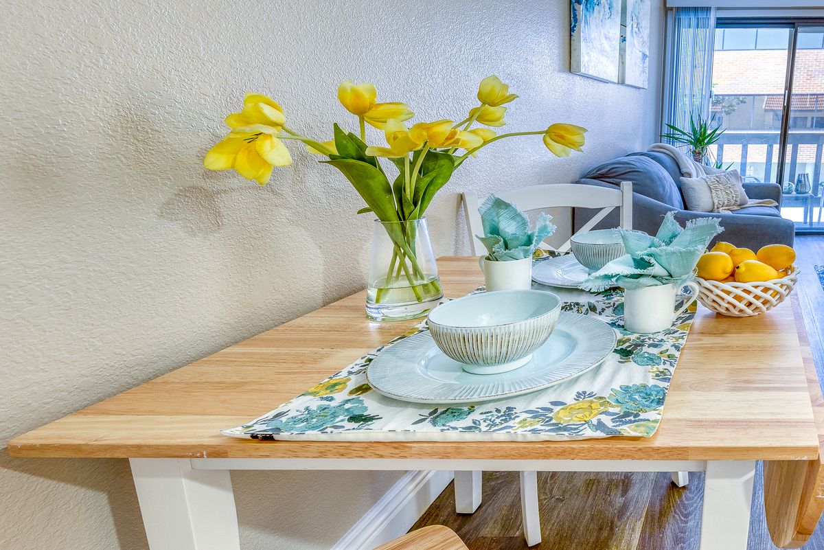 A beautifully set dining table with yellow flowers in a vase and pastel dishware.