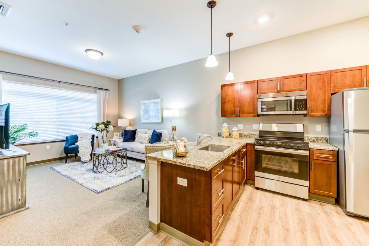 A modern open-concept living space featuring a kitchen with an island and stainless steel appliances, seamlessly connected to a cozy living area.