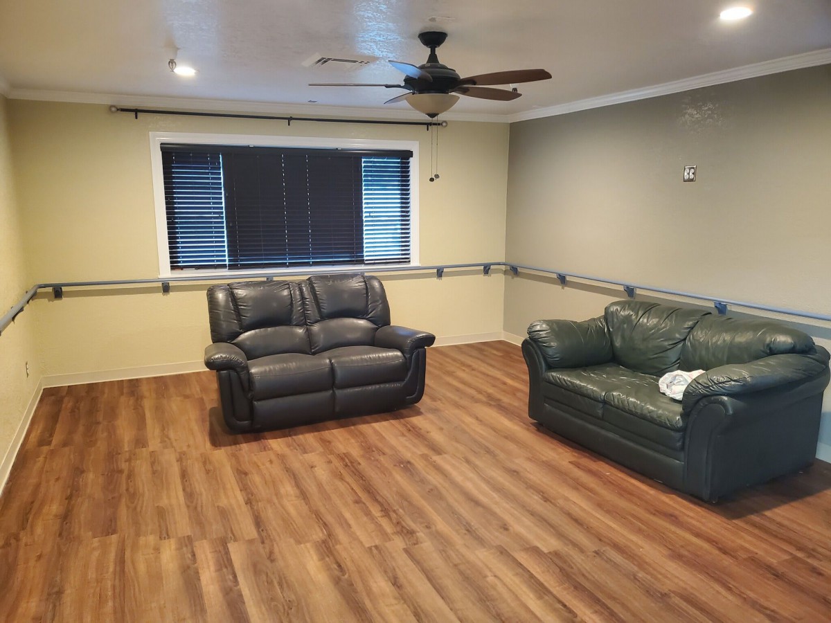 A spacious living room with wooden flooring, two sofas, a ceiling fan, and window blinds.