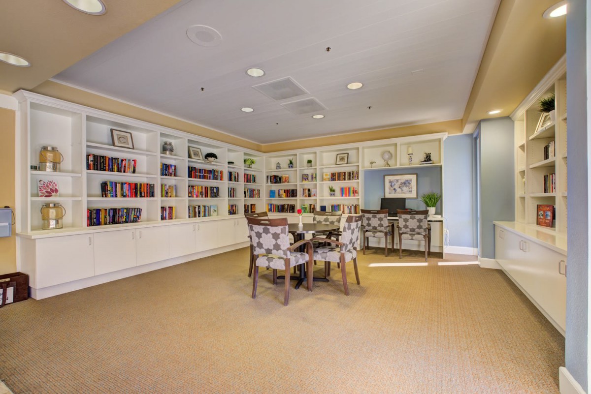 A cozy library room with built-in bookshelves, a round table surrounded by chairs, and warm lighting.