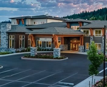 A modern commercial building with a welcoming entrance and adjacent parking lot during the evening.