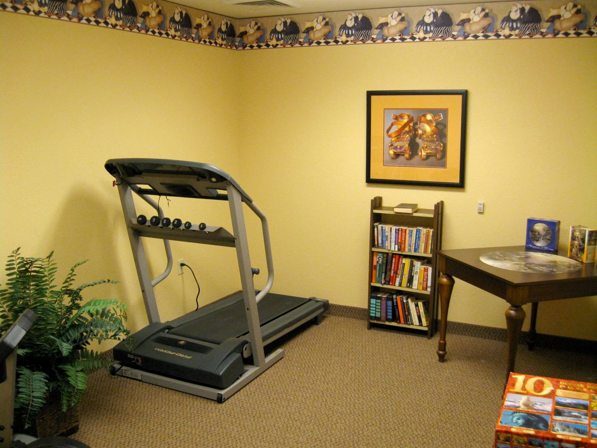 A cozy room featuring a treadmill next to a small bookshelf and artwork on the wall.