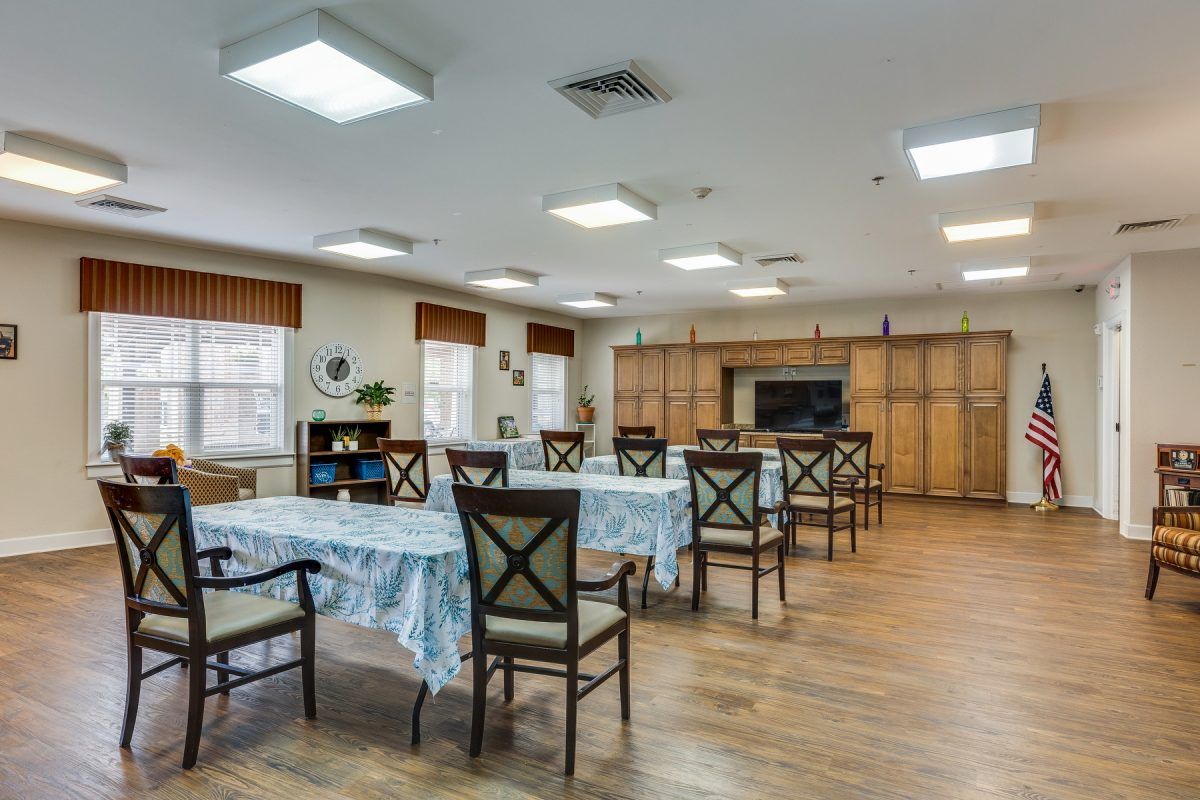 A well-lit dining area with multiple tables and chairs, featuring wooden flooring and large windows.