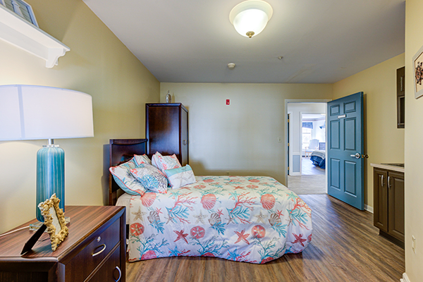 A well-lit bedroom with a colorful bedspread and wooden flooring.