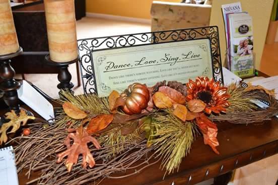 Autumn-themed home decoration with a pumpkin, leaves, and a flower arranged in front of a decorative sign.