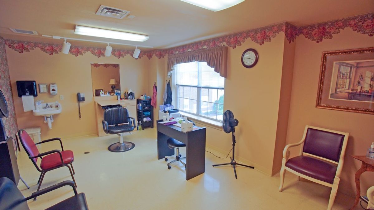 A small barbershop or salon interior with chairs, a mirror, and a desk by the window.