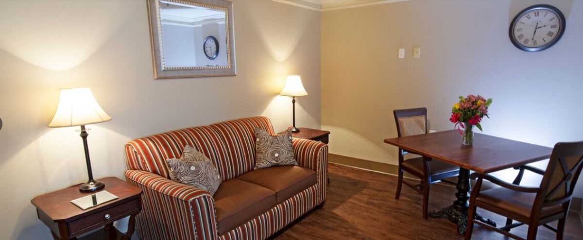 A cozy living room with a striped sofa, an elegant lamp, and a wooden table and chair.