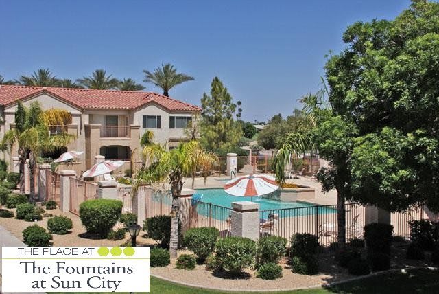 A scenic view of an apartment complex featuring a swimming pool surrounded by vibrant landscaping and palm trees.