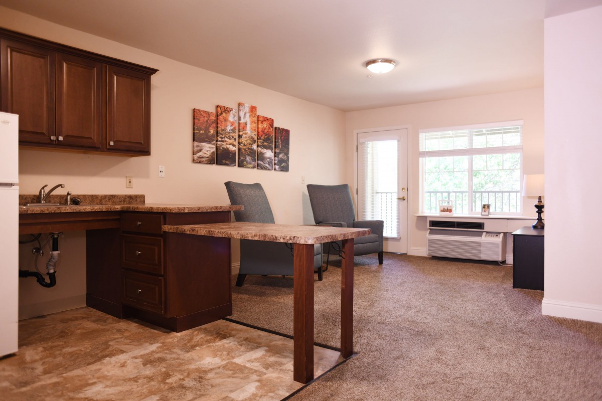 A spacious living area featuring a kitchen with a counter, comfortable seating, and natural light from large windows.