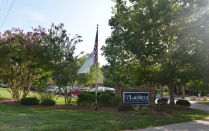 A landscaped area with a sign and flags surrounded by trees.
