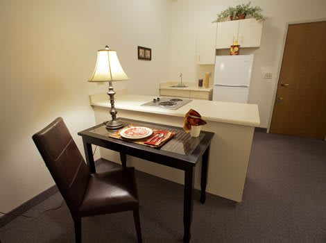 A compact kitchen and dining area with minimalist decor, featuring a small table and chair next to a lamp.