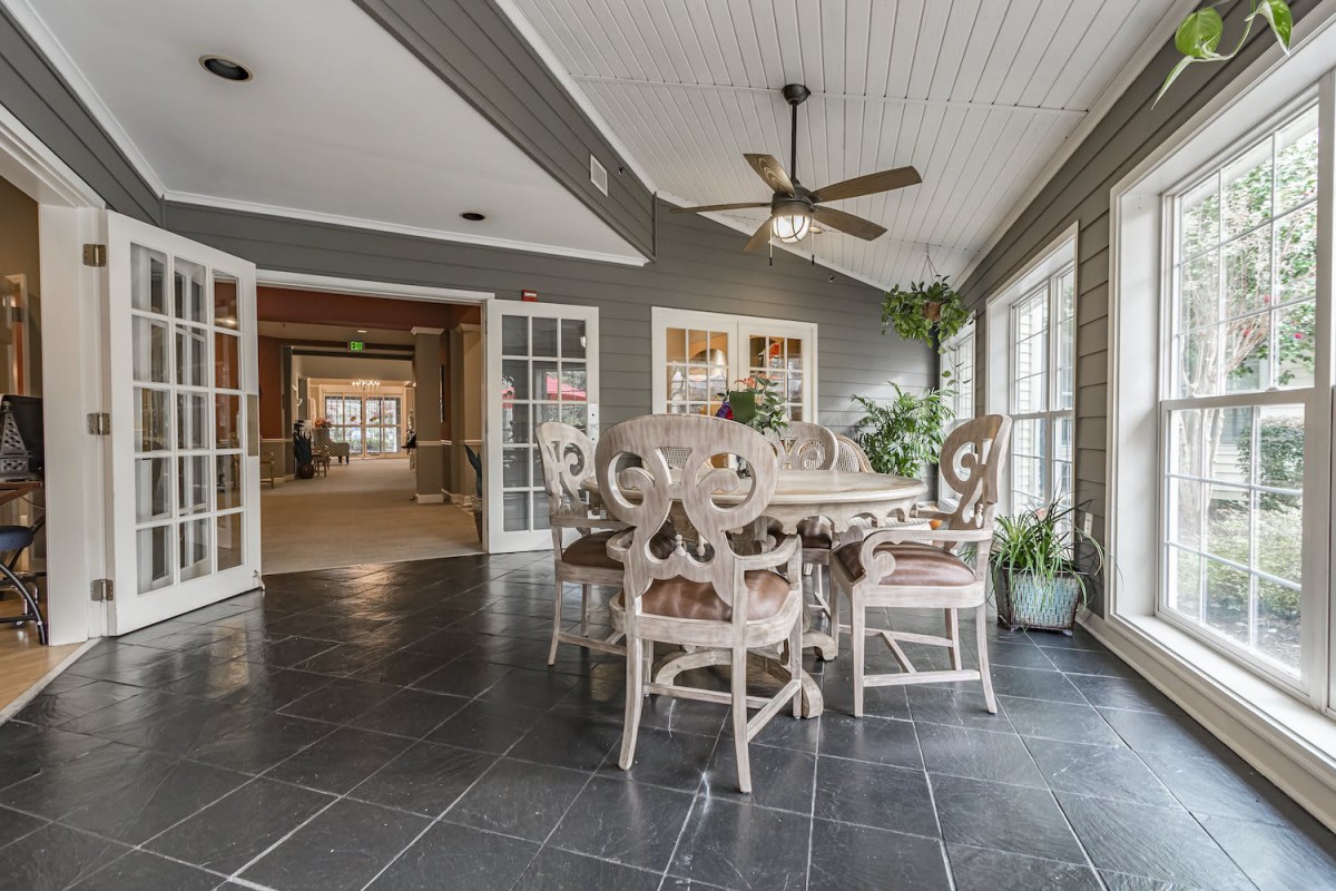 A bright dining area with elegant furniture, ceiling fan, and large windows offering natural light.