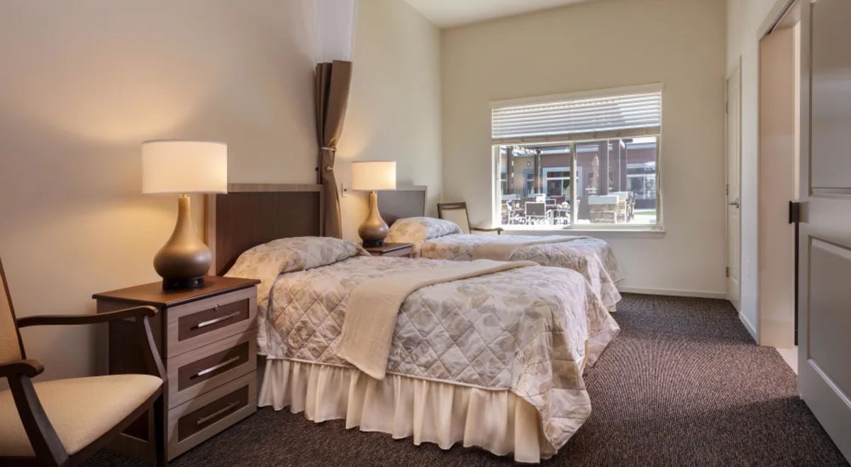 A cozy bedroom featuring twin beds with floral bedding, bedside lamps, and a large window.