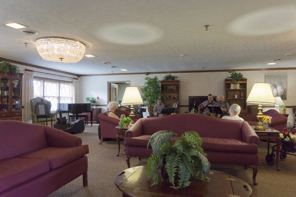 A cozy living room with multiple sofas, a chandelier, and people seated around.
