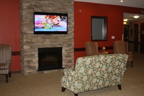 A cozy living room with a stone fireplace, television mounted above, and comfortable seating.