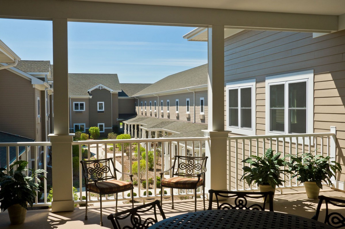 A cozy patio overlooking a building with outdoor seating and lush greenery.