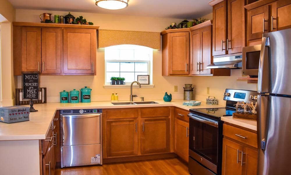 A cozy kitchen with wooden cabinets and stainless steel appliances, featuring a bright window and decorative plants on the countertops.