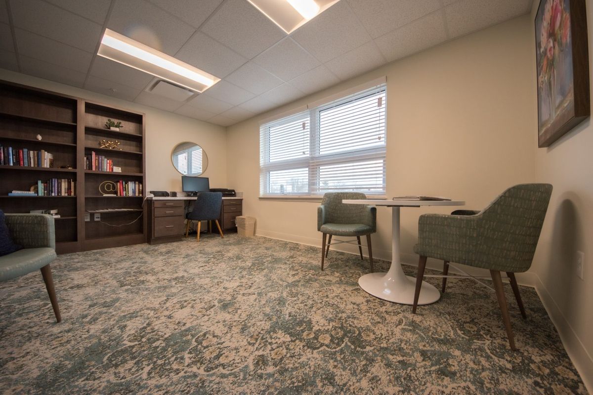 A cozy office space featuring a desk, bookshelf, and seating area with a table near the window.
