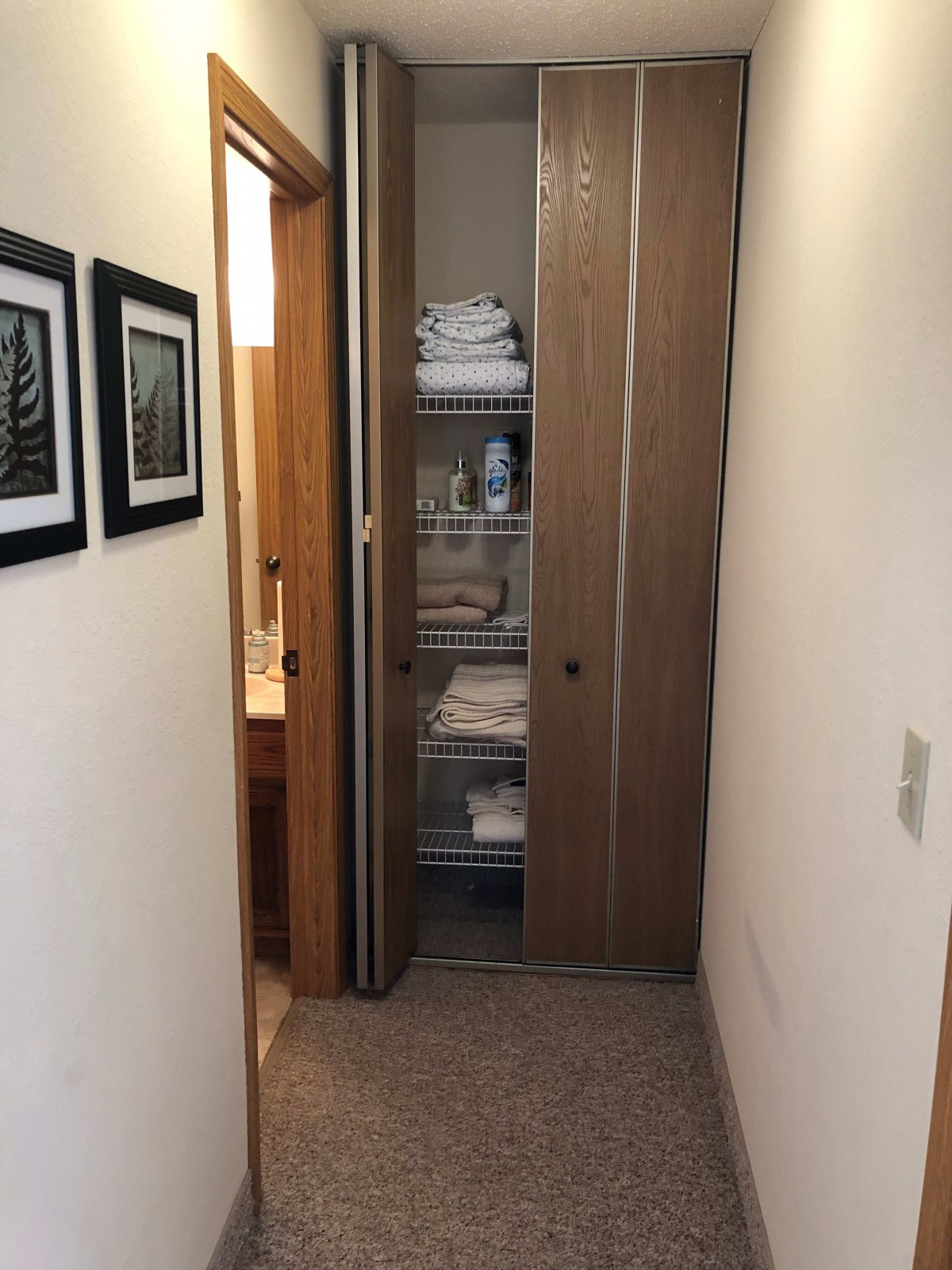 A hallway with a linen closet filled with neatly folded towels and other items.