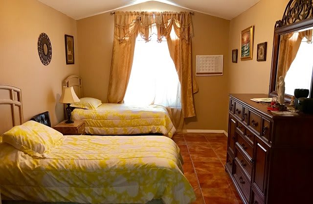 A cozy bedroom with two single beds, warm decor, and a window with curtains.