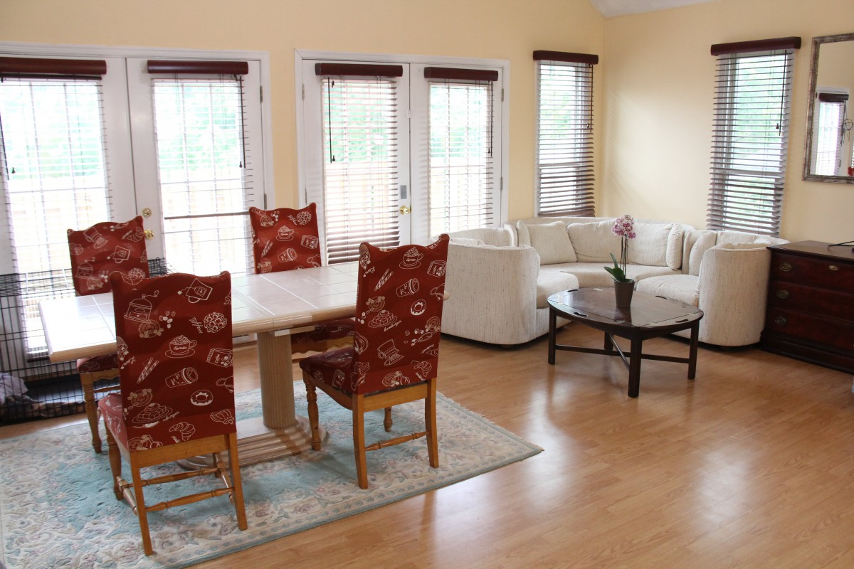 A bright and airy living room with a dining area, featuring wood flooring, large windows, and comfortable seating.