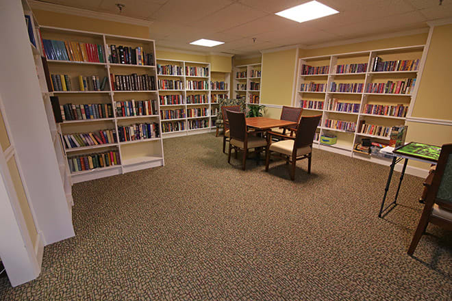 A quiet library room with bookshelves and a reading table surrounded by chairs.
