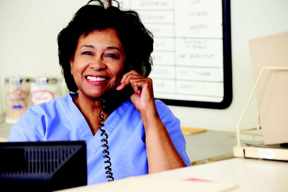 A woman in a uniform smiling while talking on the phone at her workspace.