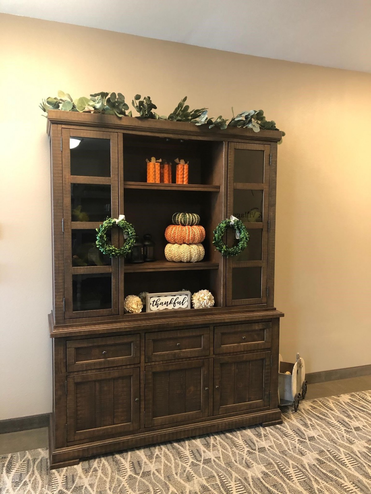 A wooden cabinet decorated with autumn-themed items including pumpkins and wreaths.