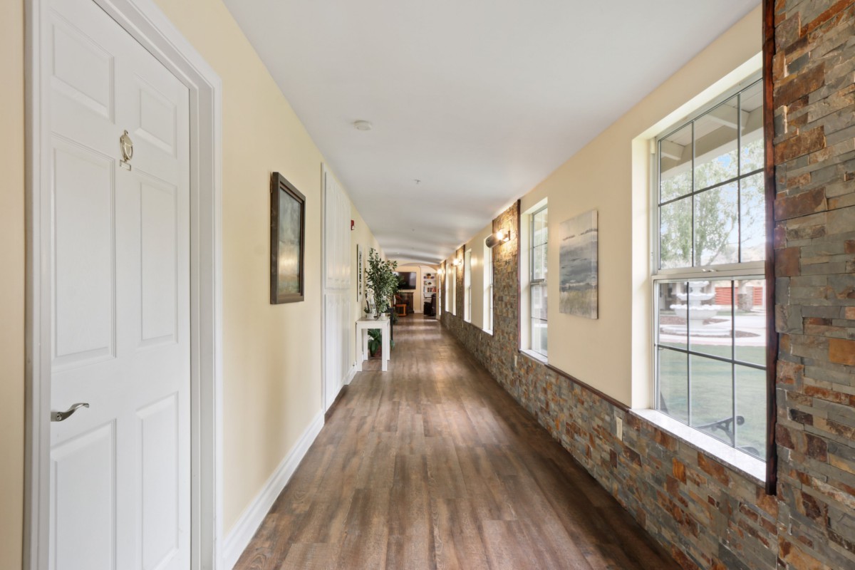 A long, well-lit hallway with wooden floors and large windows.