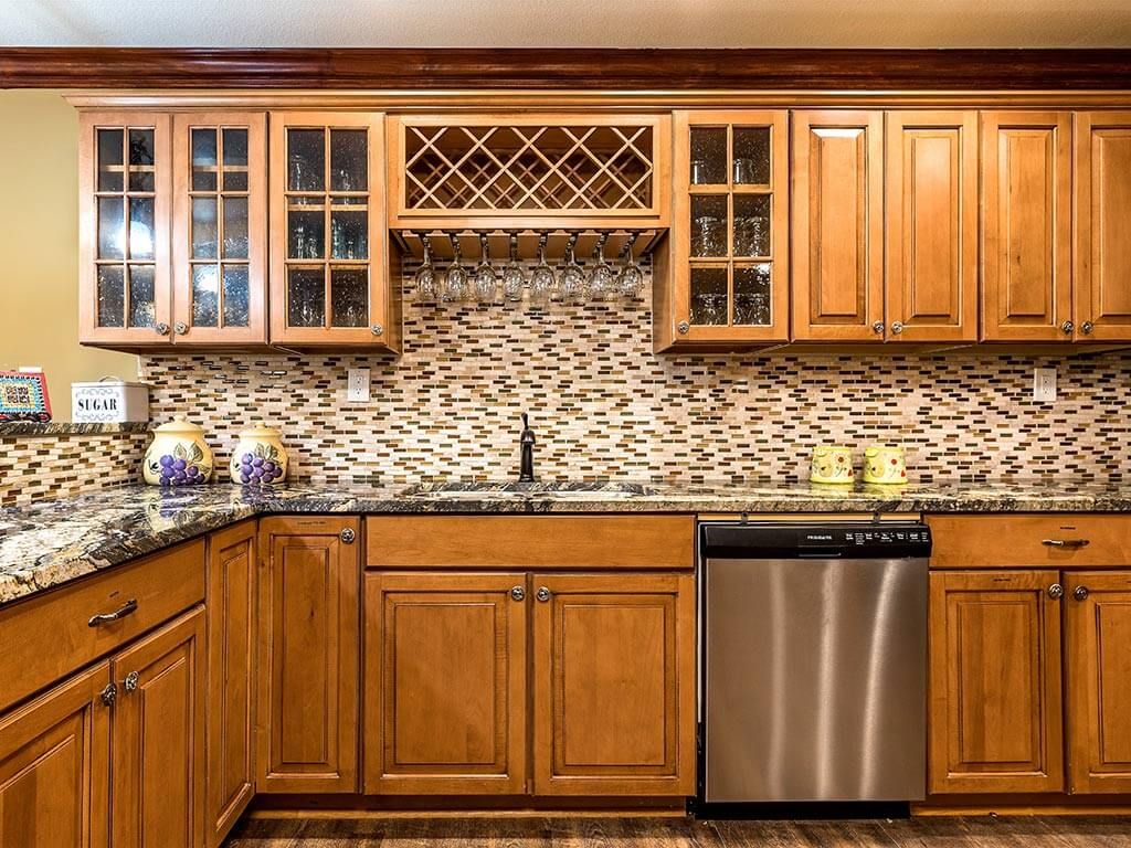 A cozy kitchen featuring wooden cabinets, a patterned backsplash, granite countertops, and a stainless steel dishwasher.
