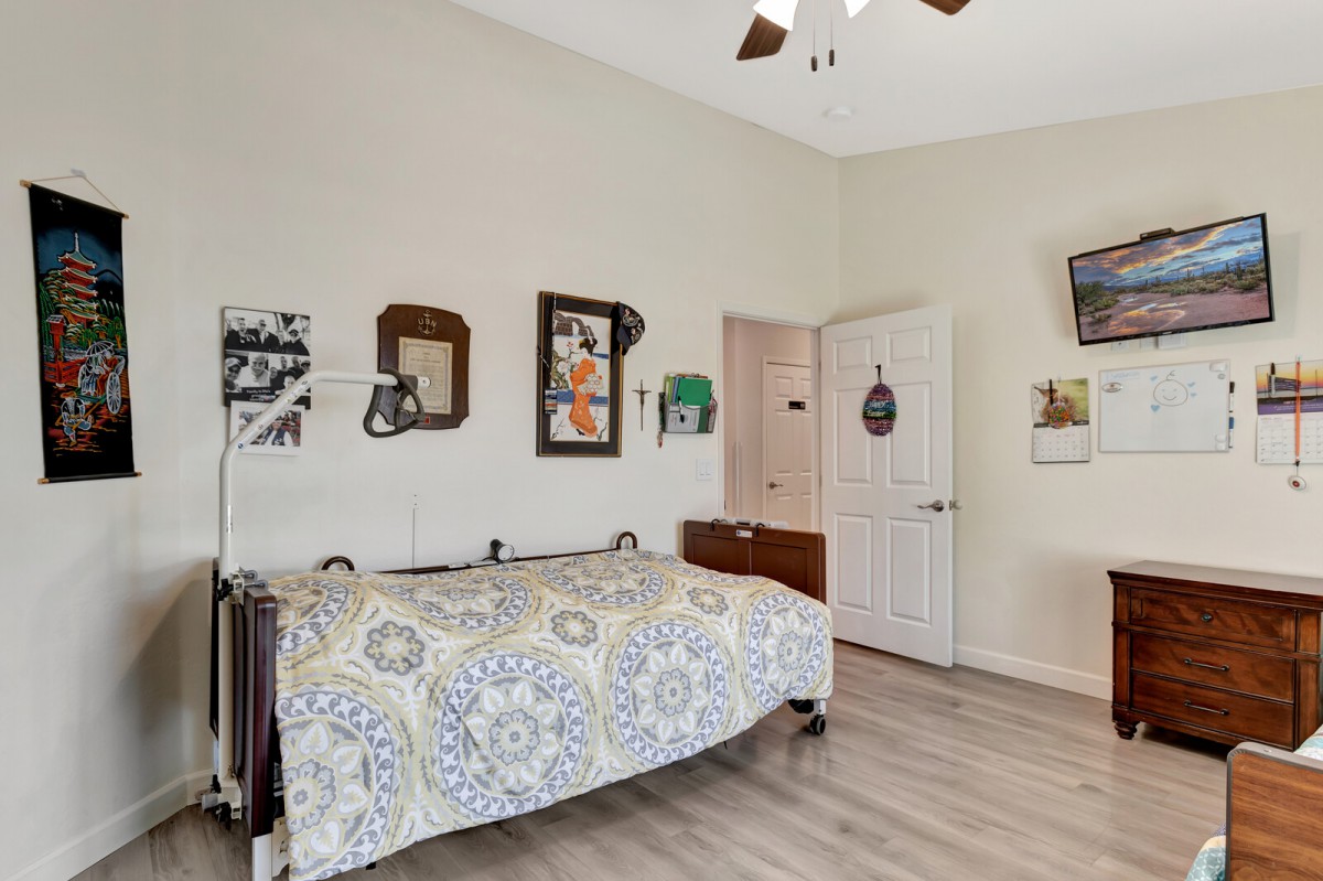 A cozy bedroom featuring a bed with patterned bedding, wall art, a ceiling fan, and wooden flooring.