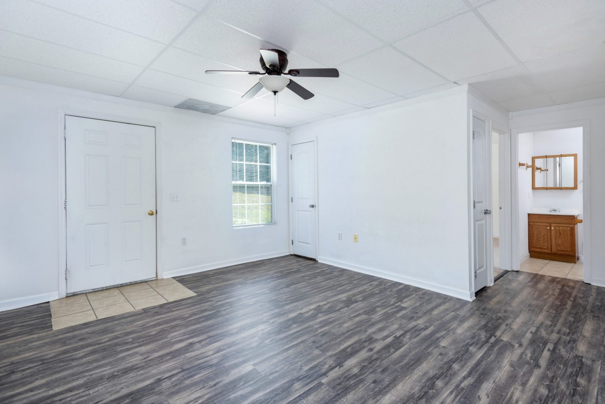 An empty room with wood flooring, a ceiling fan, and white walls.