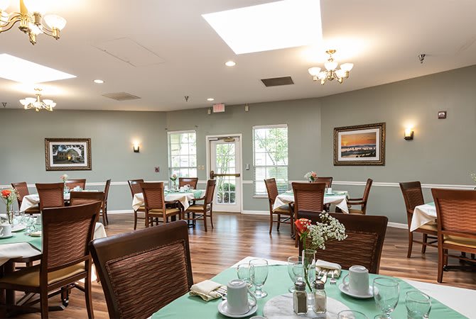 A well-lit dining room with neatly arranged tables and chairs, featuring elegant decor and large windows.