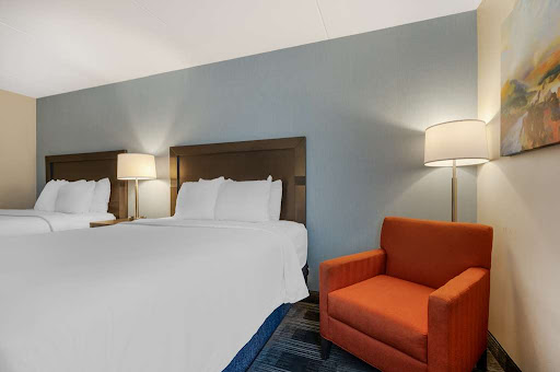 A cozy hotel room featuring two beds, an orange armchair, and stylish lighting.