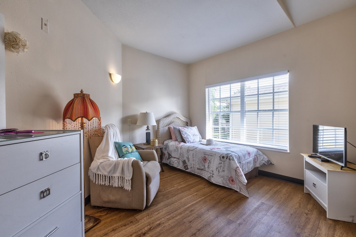 A cozy bedroom with a single bed, armchair, and large window allowing natural light to brighten the space.