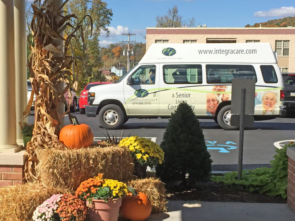 A decorated outdoor display with pumpkins, flowers, and hay bales in front of a parked van on an autumn day.