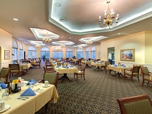 An elegant dining room with neatly set tables and chandeliers overhead.