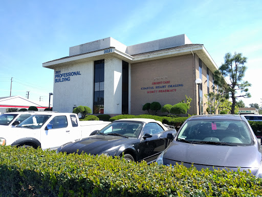 A commercial office building with vehicles parked in front and greenery surrounding the area.
