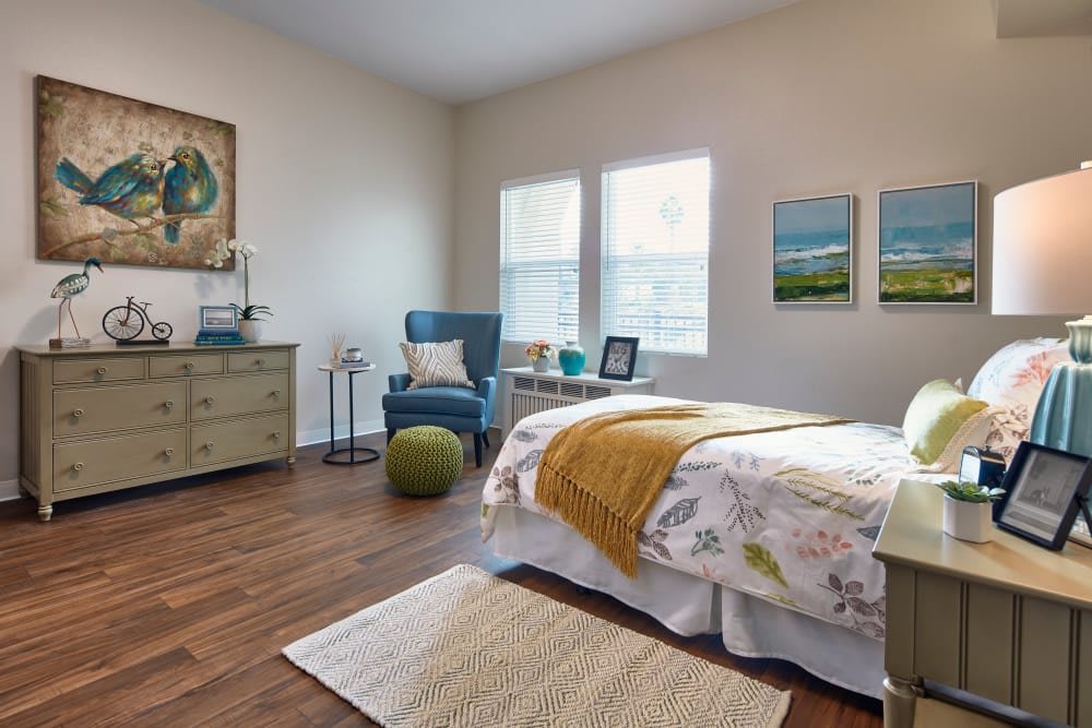 A cozy and well-decorated bedroom with a bed, armchair, dresser, and two windows.
