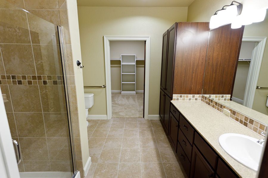 A modern bathroom with a shower, sink, and cabinets featuring tile flooring.